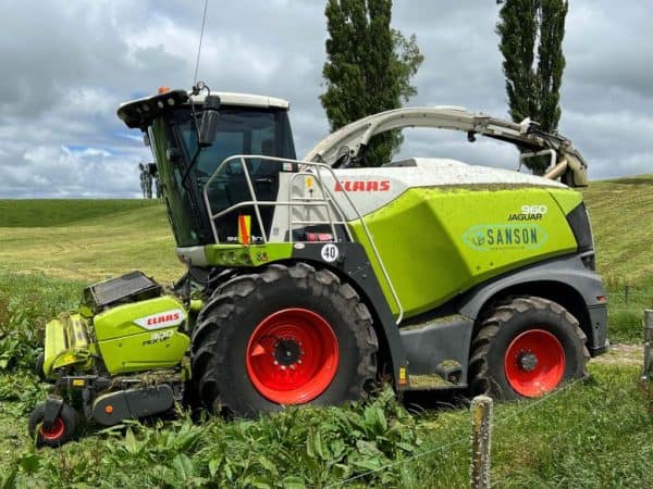 Claas Jaguar forage harvester with Sanson branding working in lush green paddock.