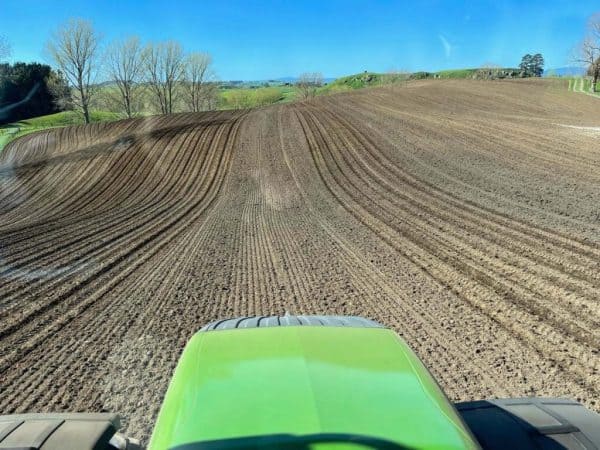 Tractor preparing rich farmland for planting in a lush New Zealand landscape.
