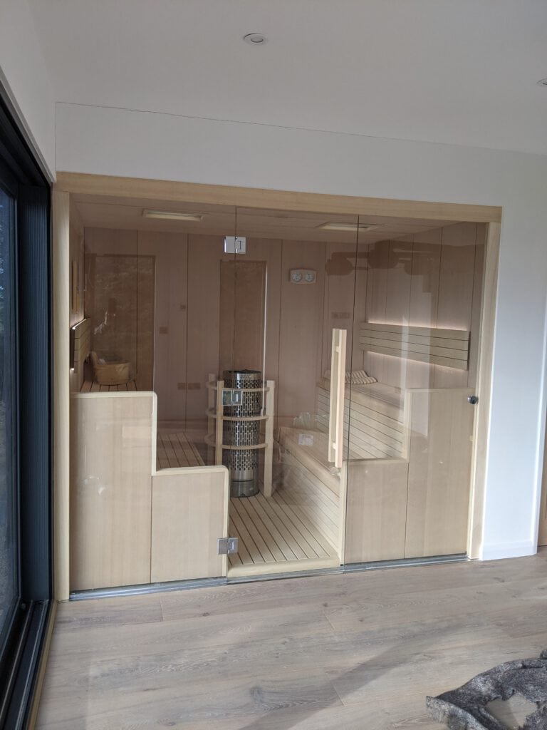 A detailed, modern indoor sauna with a glass door and wooden interior