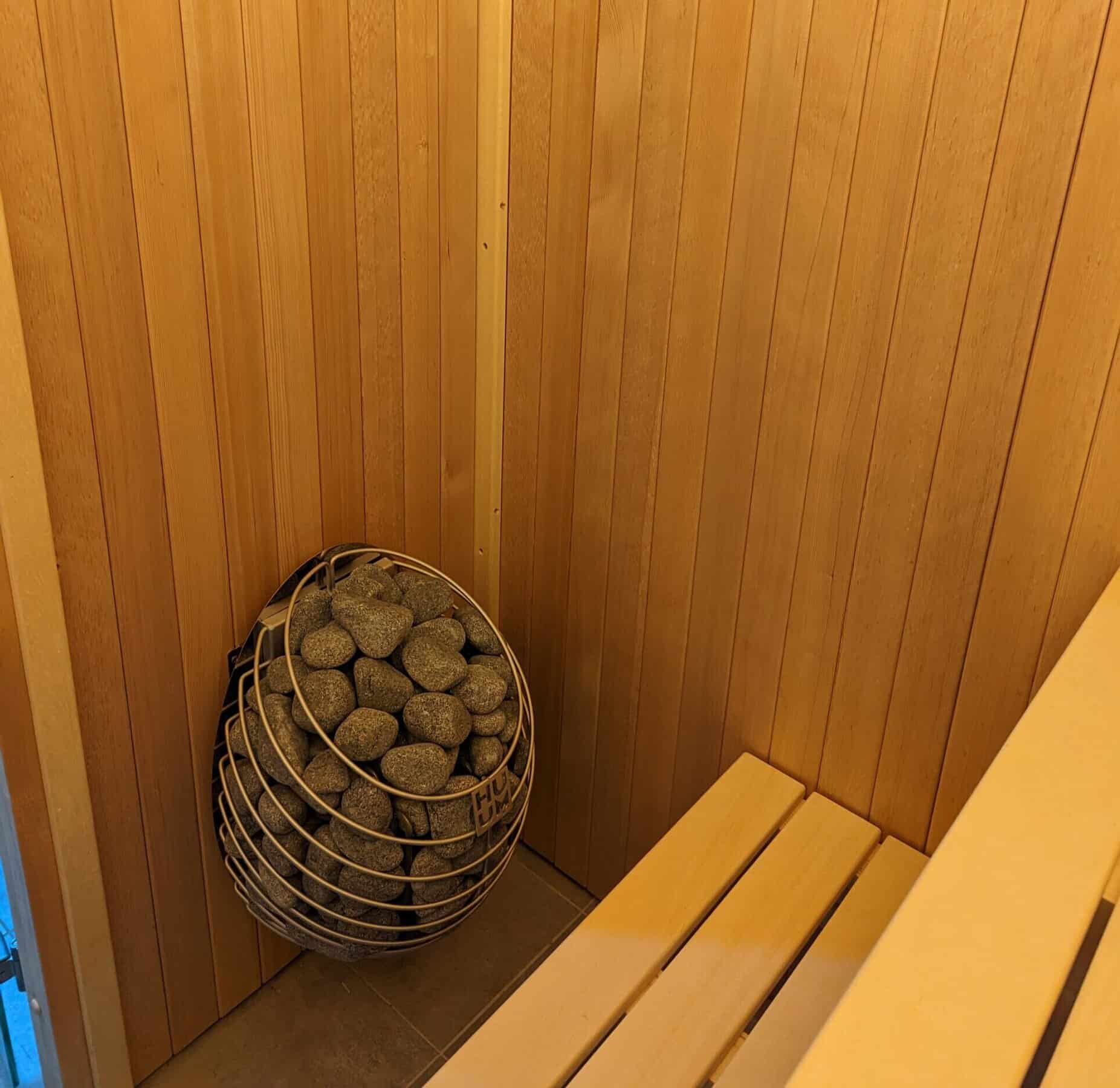 wooden sauna interior with a traditional heater filled with sauna stones.