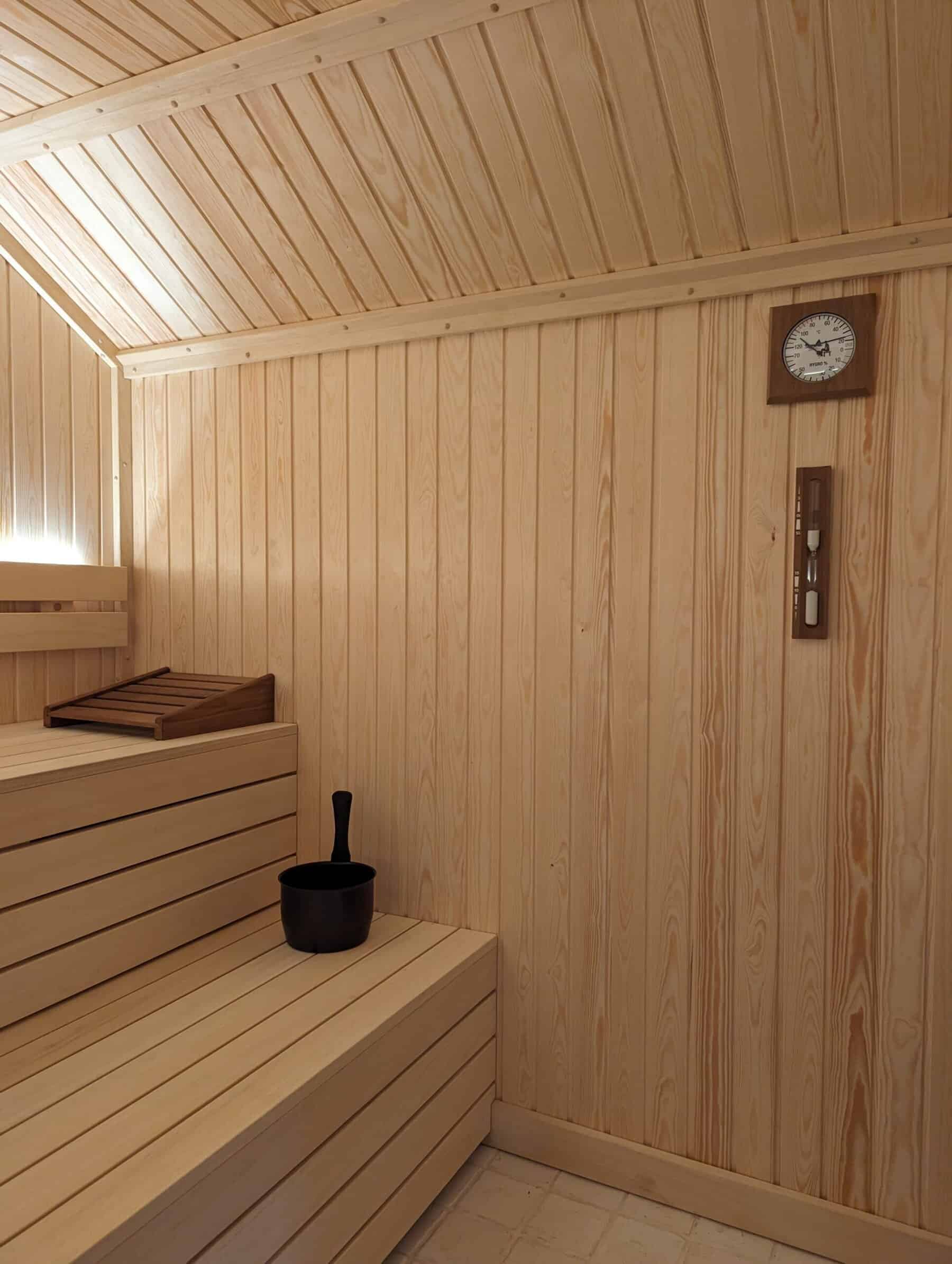 Wooden sauna interior with a traditional heater and timer, showcasing natural light and warm tones.