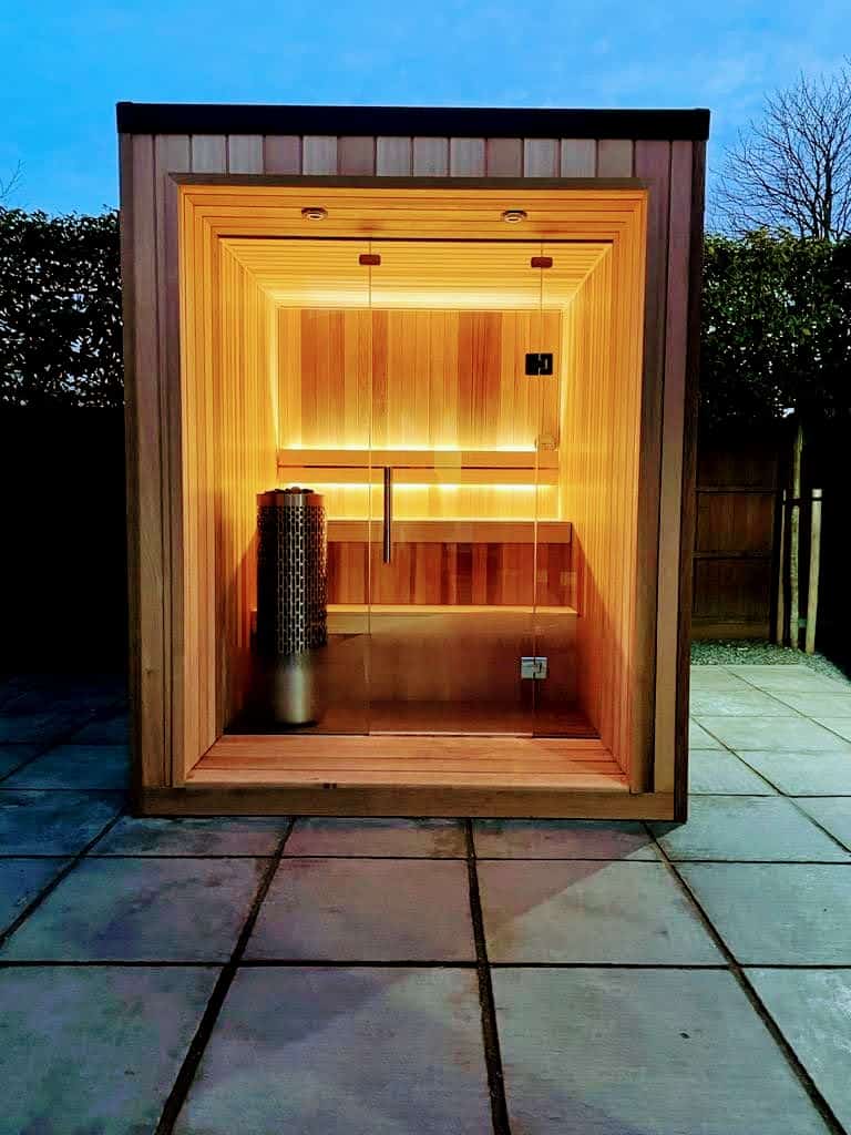Relaxing outdoor infrared sauna cabin with wooden interior, warm lighting, and glass door.