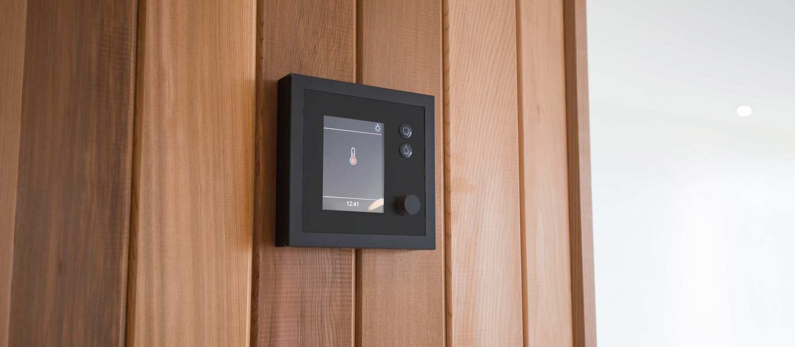 A detailed image of a modern sauna control panel mounted on wooden paneling, used to regulate sauna temperature and settings.