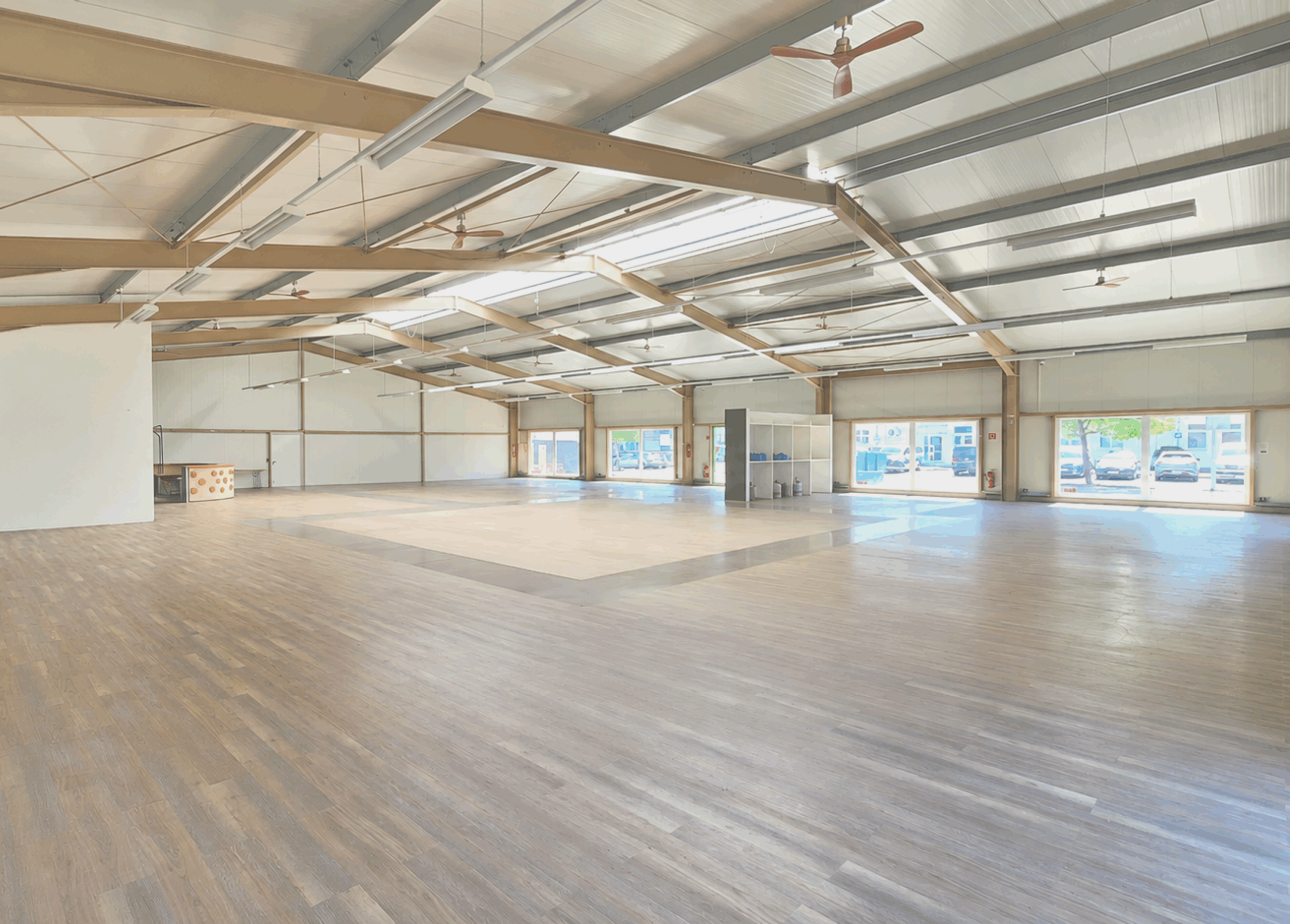Geräumige Gewerbehalle mit Holzfußboden, große Fenster und offene Decke, ideal für Unternehmen.