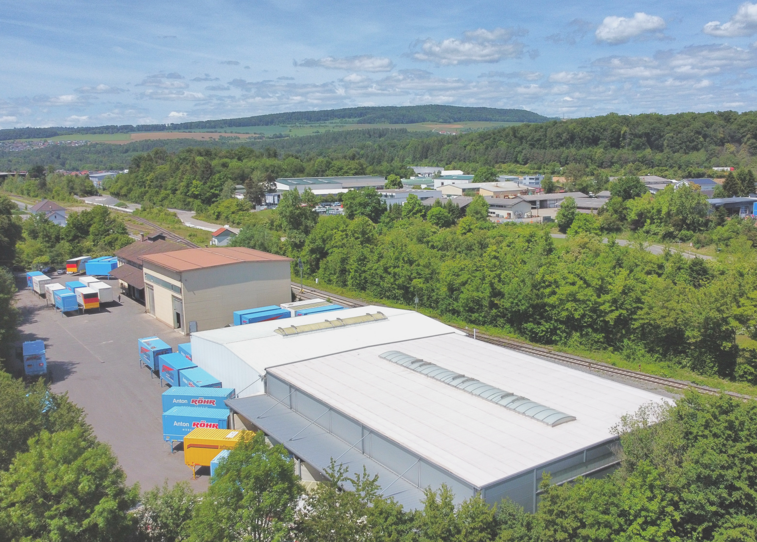 Logistikzentrum mit Lagerhallen und LKWs in grüner Umgebung, bei Schlatter Immobilien GmbH.