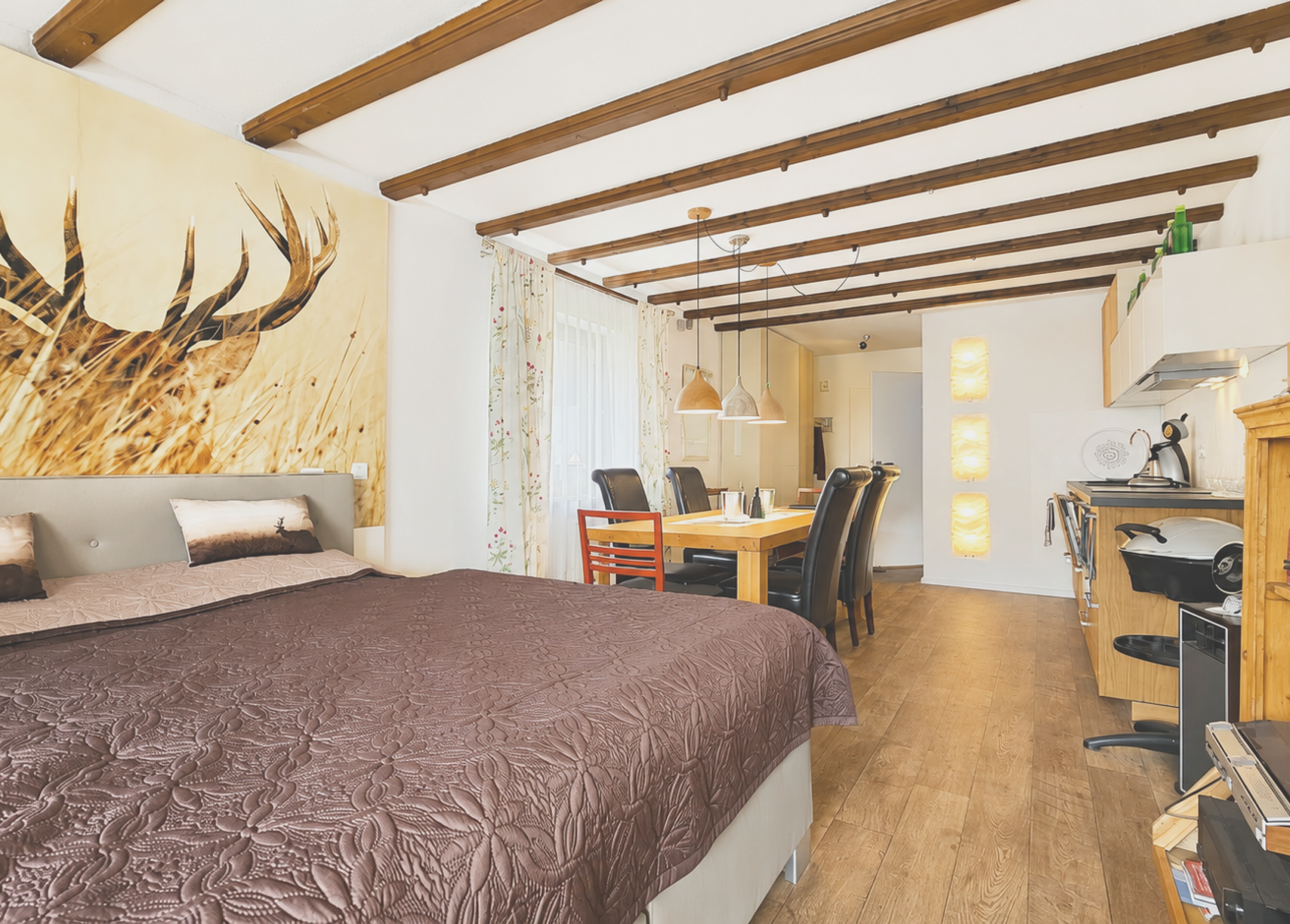 Helles Schlafzimmer mit rustikalem Holzdecke und offener Küche im Hintergrund.