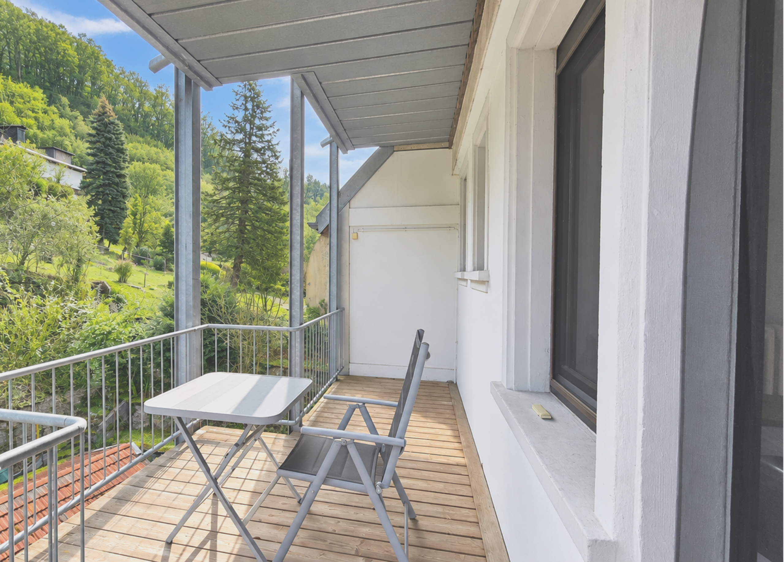 Balkon mit Tisch und Stühlen, Blick ins Grüne, bei Sonnenschein.