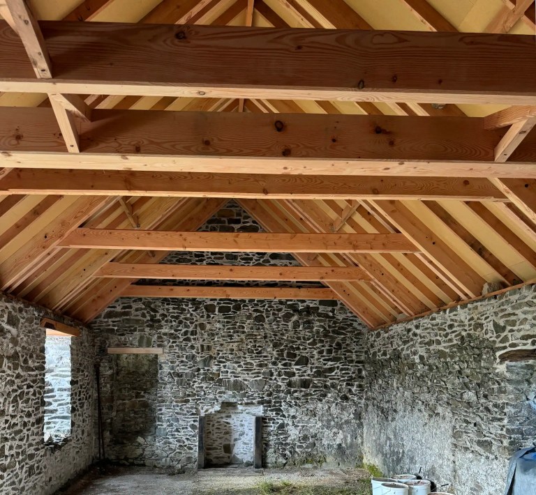 Indoor view of a new roof with thick beams over an old stone walled cottage