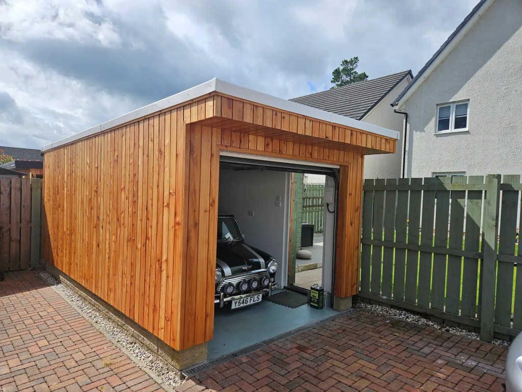 Exterior of garage clad with shadow gap larch cladding, housing a classic car