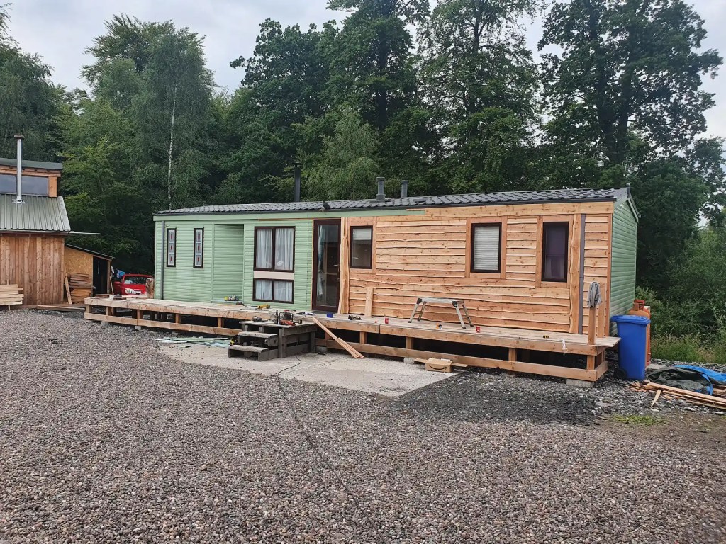 Outside of caravan that is in process of being covered with larch waney edge cladding