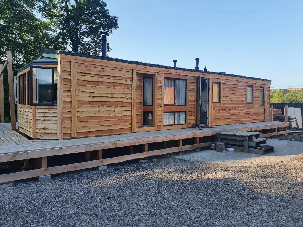 Outside of a static caravan that has been finished with larch waney edge cladding, giving it the look of a timber cabin