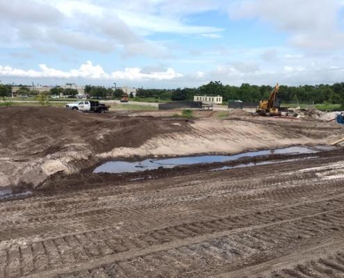 Excavation site for commercial development with heavy construction equipment and ongoing land grading in progress.