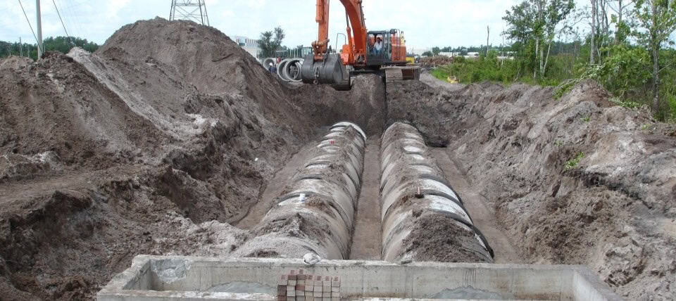 Heavy equipment installing large underground pipes for infrastructure development in a construction site.