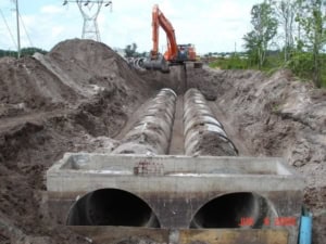 Heavy construction site with large sewer pipes being installed for infrastructure development, showcasing trench excavation for underground utility installation.