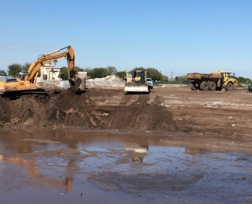 Excavators and construction vehicles working on site development, site prep, and land clearing for commercial or industrial project in progress.