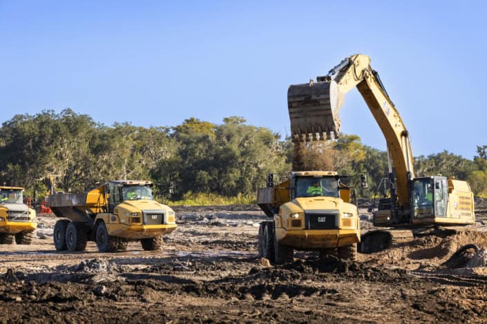 Excavator and construction trucks working on land development for commercial or industrial site preparation.