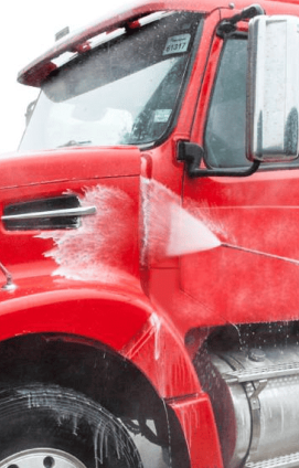 A red dump truck is washed with a pressure washer as part of fleet vehicle detailing