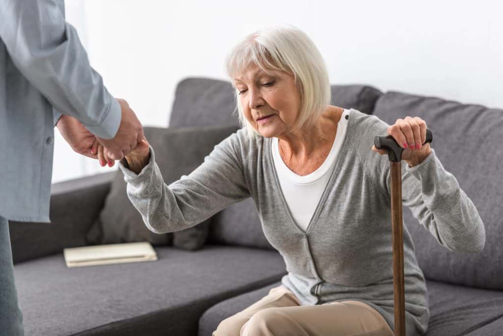 An older lady receiving help from a carer to stand up