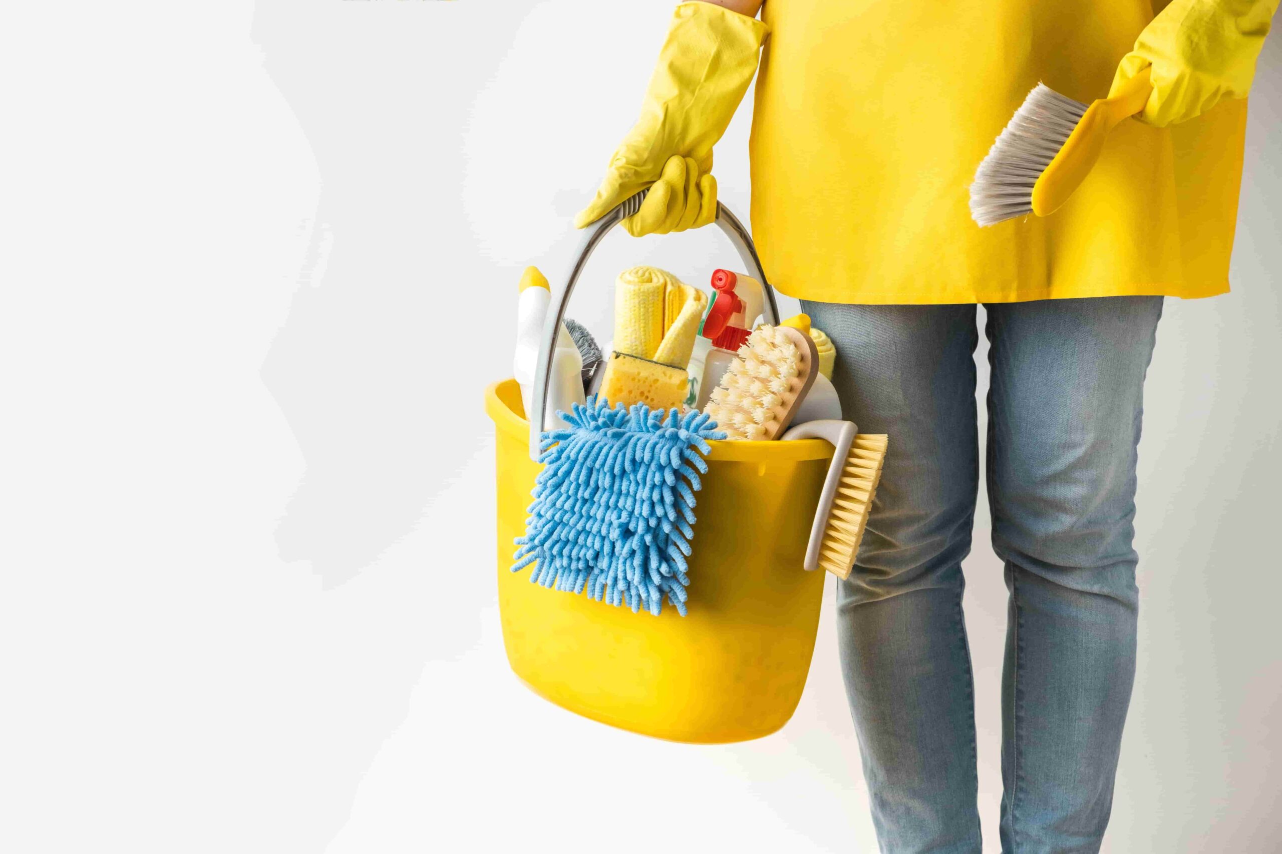 A person holding a yellow bucket filled with cleaning supplies, including mops, brushes, and sprays, demonstrating professional cleaning tools.