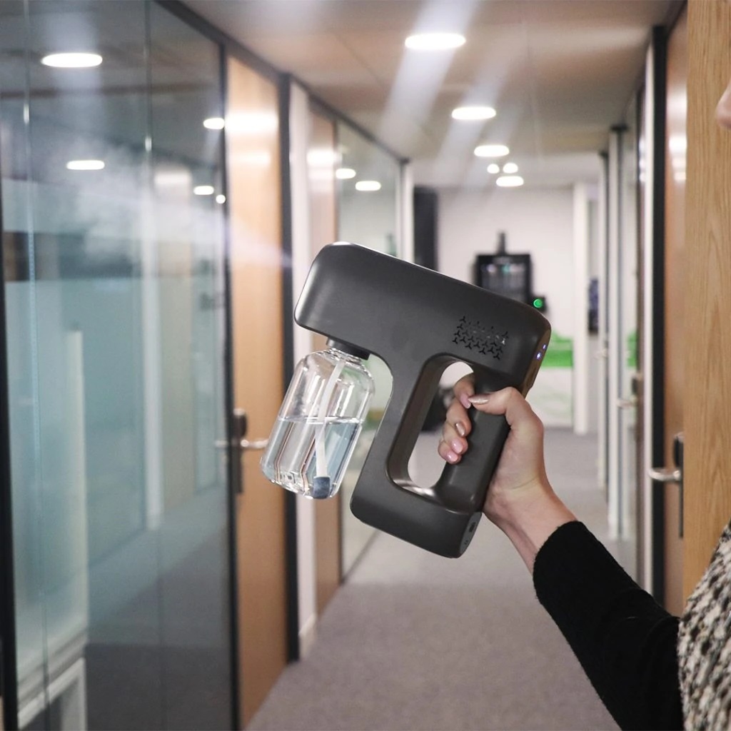 Hand holding a sanitising disinfectant spray gun in an office corridor.