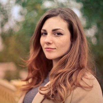 A woman with brunette hair and freckles standing outside, wearing a grey shirt with a tan cardigan