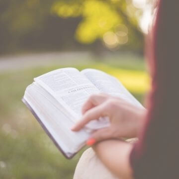 woman in red top reading bible outdoors in sunshine