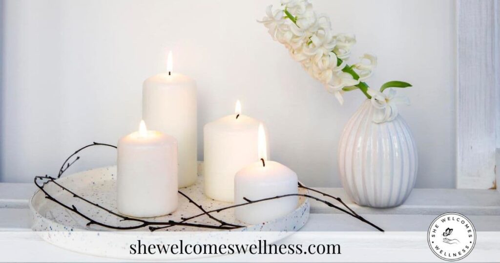Three lit white candles on a speckled tray beside a white vase with delicate flowers