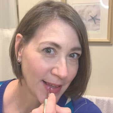 Tina putting on lip gloss as part of a clean beauty routine.