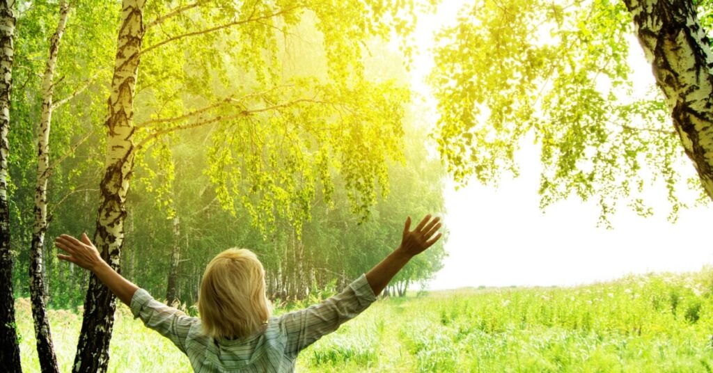 woman in nature raising her hands towards the sunlight
