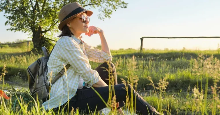 Woman in sunglasses and hat sitting in nature-self-care-tips-for-balance