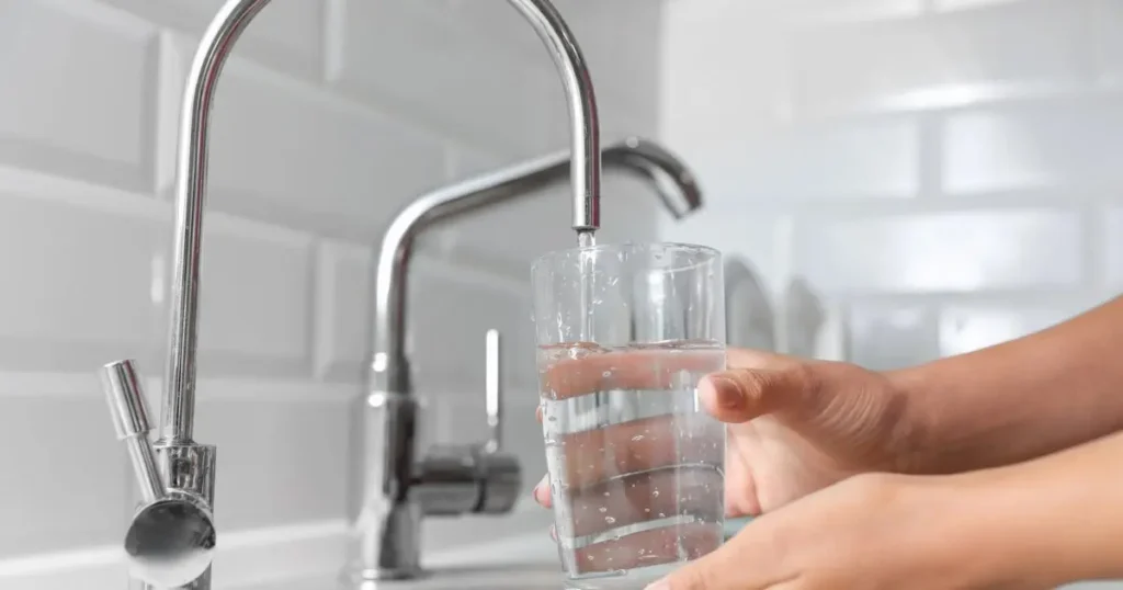 Woman pouring filtered water into glass in kitchen, closeup

