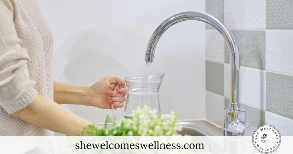 A person fills a clear glass pitcher with water from a kitchen faucet water filter. The scene is bright, with a peaceful atmosphere, emphasizing cleanliness.