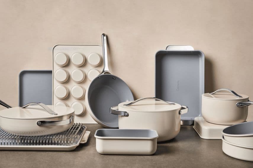 Elegant cream-colored Caraway non-toxic cook and bake set with pots, pans, baking trays, and muffin tin arranged neatly on a neutral background, conveying a modern, minimalist style.