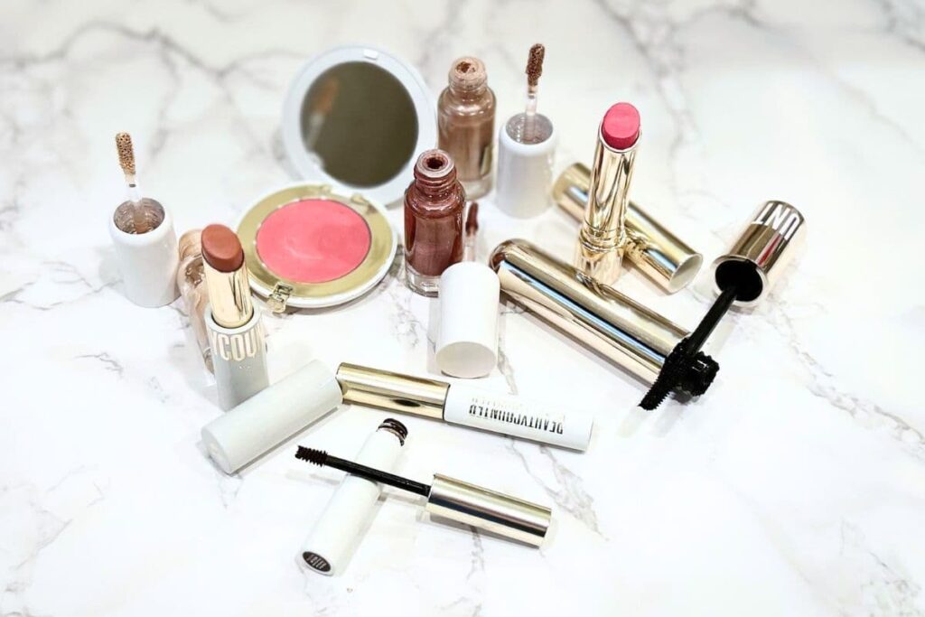 Beautycounter September 2025 clean makeup launch products — Think Big Mascara, Brilliant Brow Gel, Lid Glow Cream Shadow, Clean Swipe Lip Balm, plus lipstick and blush — flat lay on a marble surface.