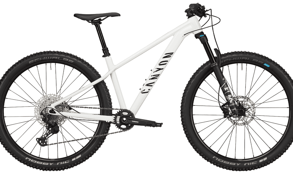 White mountain bike with front suspension, disc brakes, and knobby tires for trail riding.