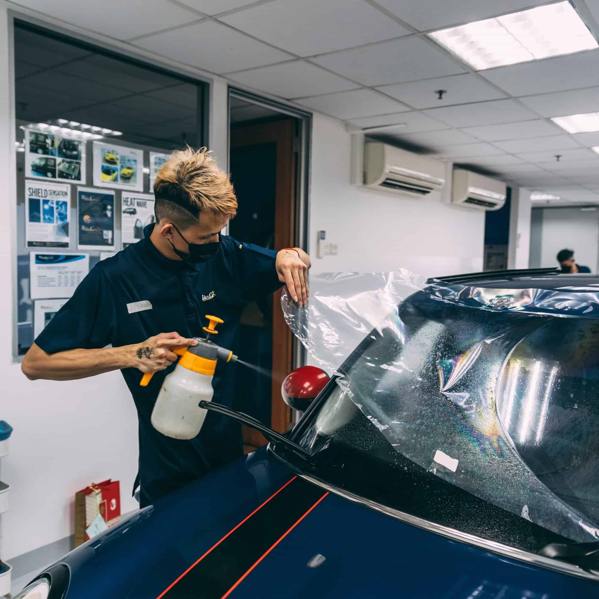 A technician applies protective films to a car's windshield and headlamp to prevent stone chips and.