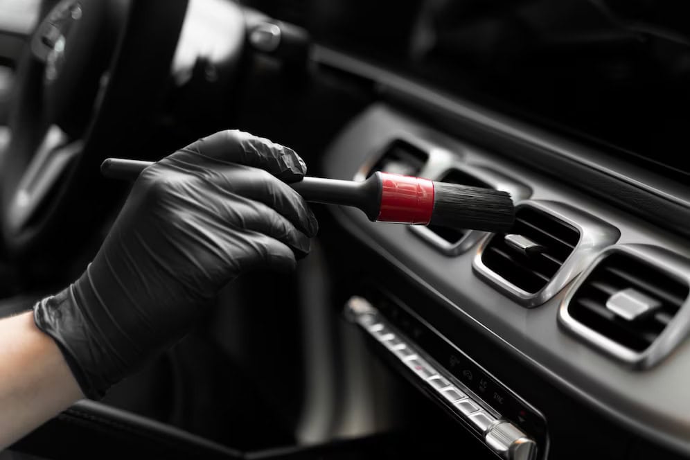 Technician applying detailing polish to car interior vents with a brush.