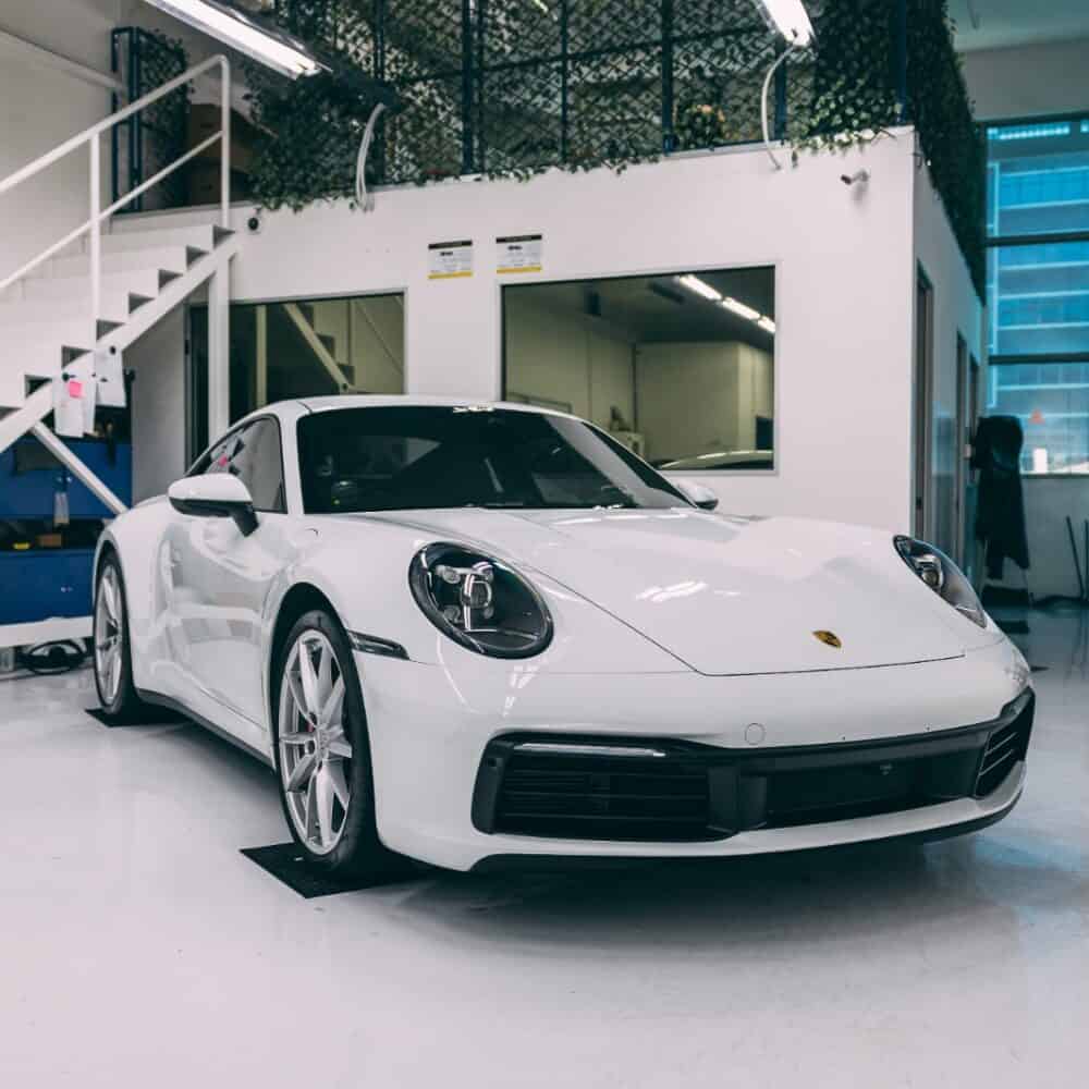 White Porsche sports car inside detailing workshop with equipment.