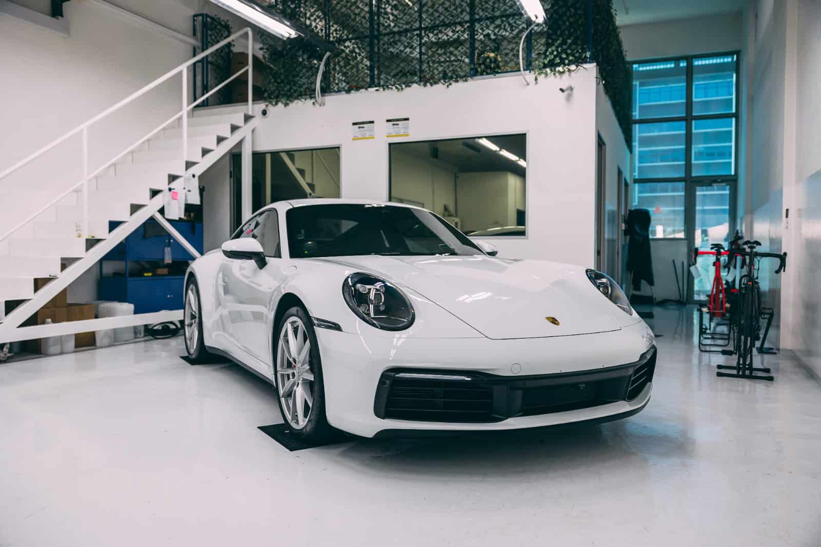 White Porsche sports car inside detailing workshop with equipment.