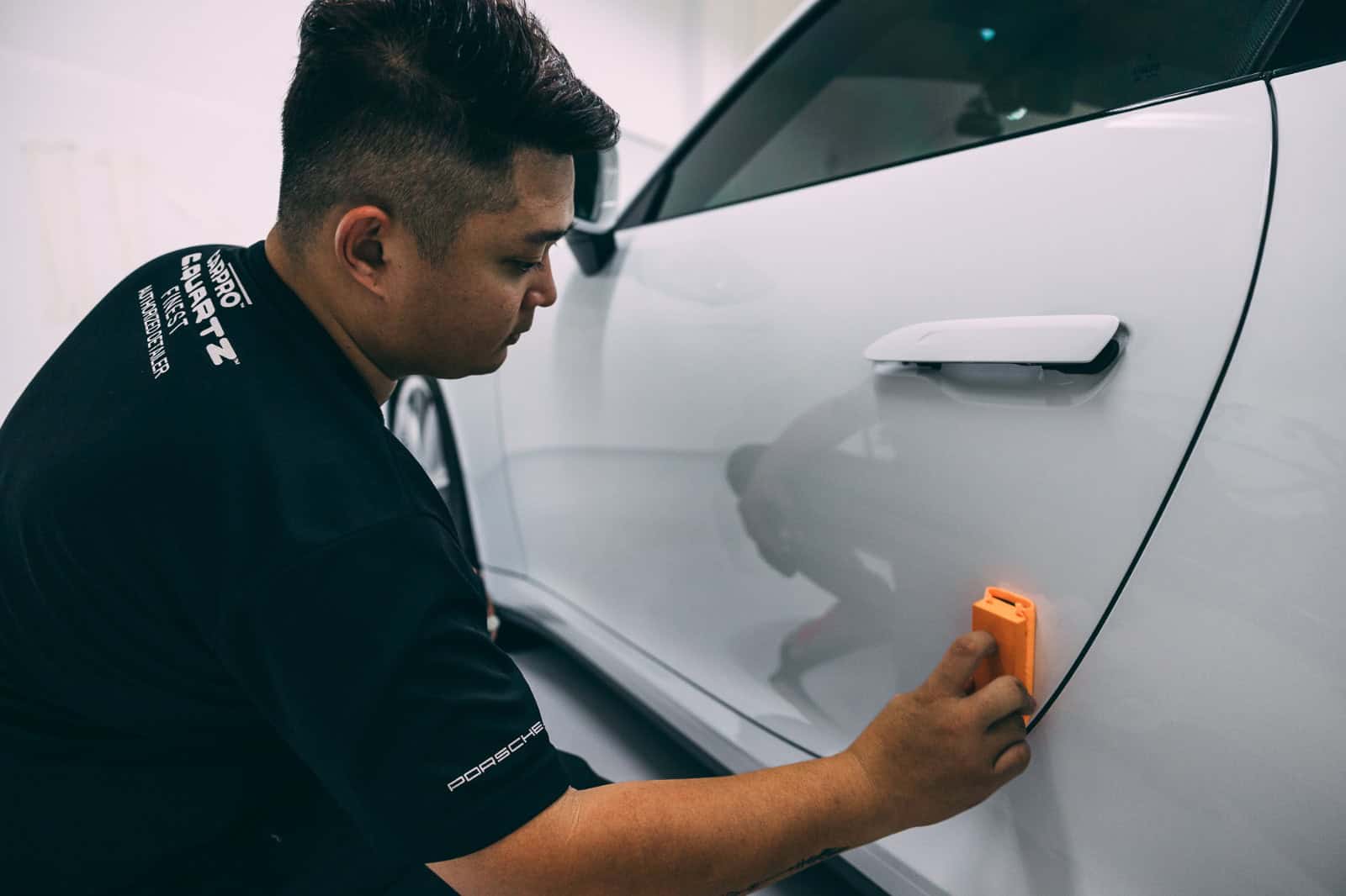 Technician applying PPF film on white car door for protection and finish.