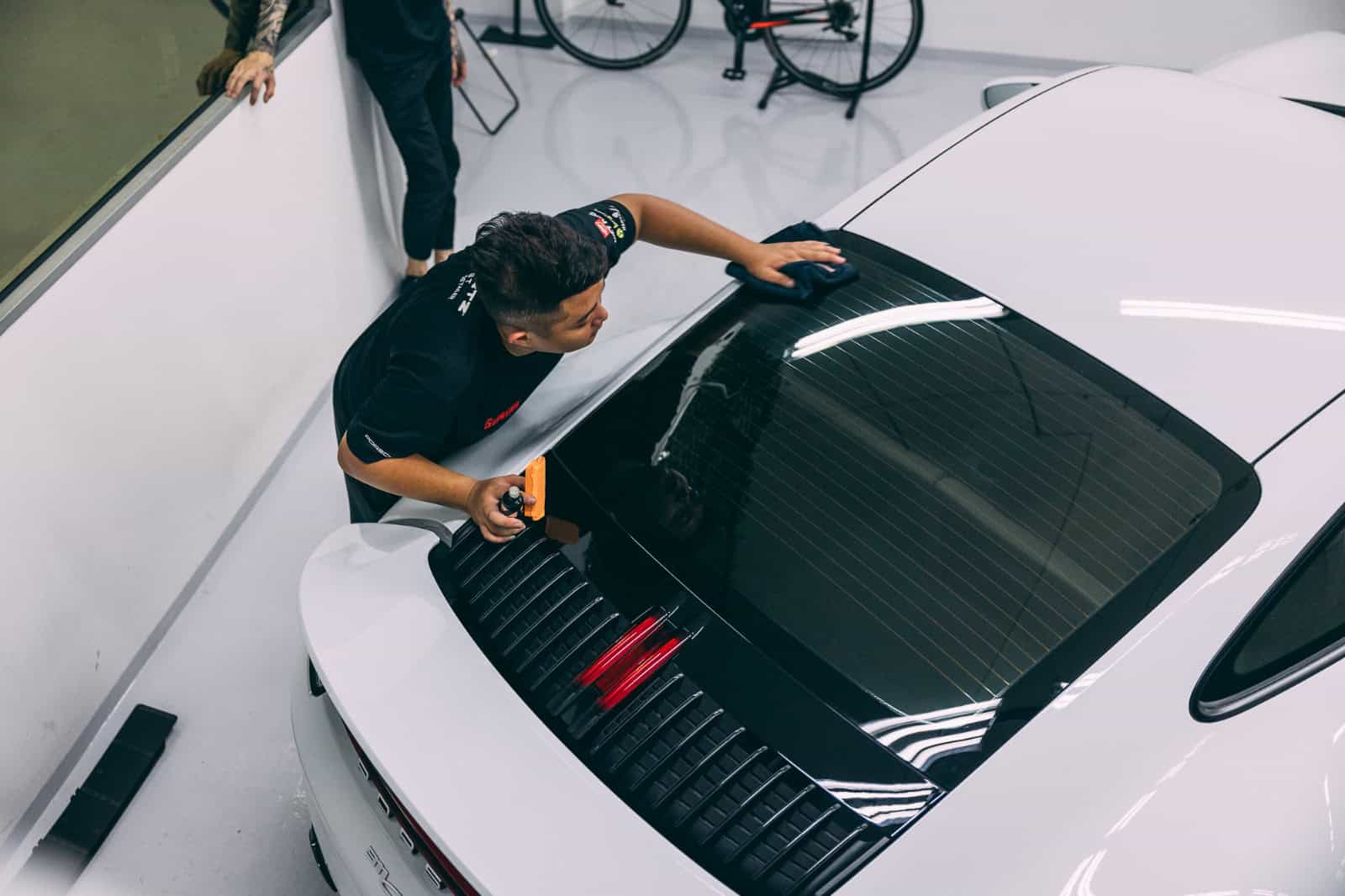 Technician applying paint protection film on a white sports car during full detailing.