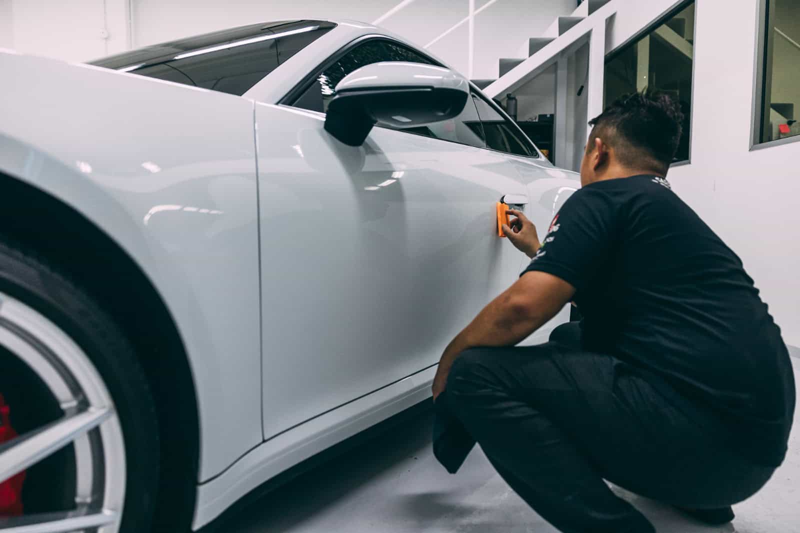 Technician applying paint protection film to a white car during pre-installation detailing.