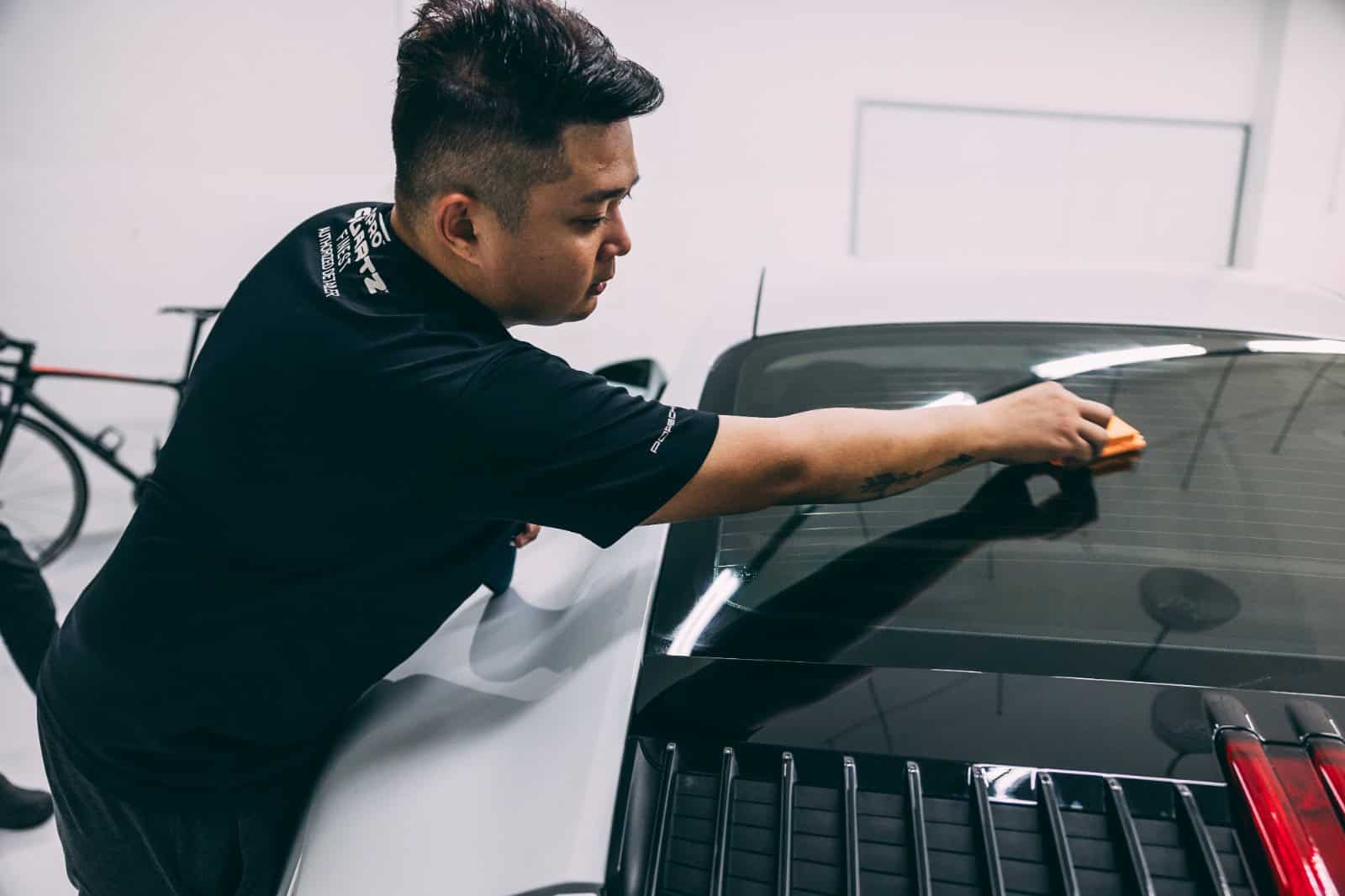 Car detailing technician applying PPF on vehicle's hood and windshield.