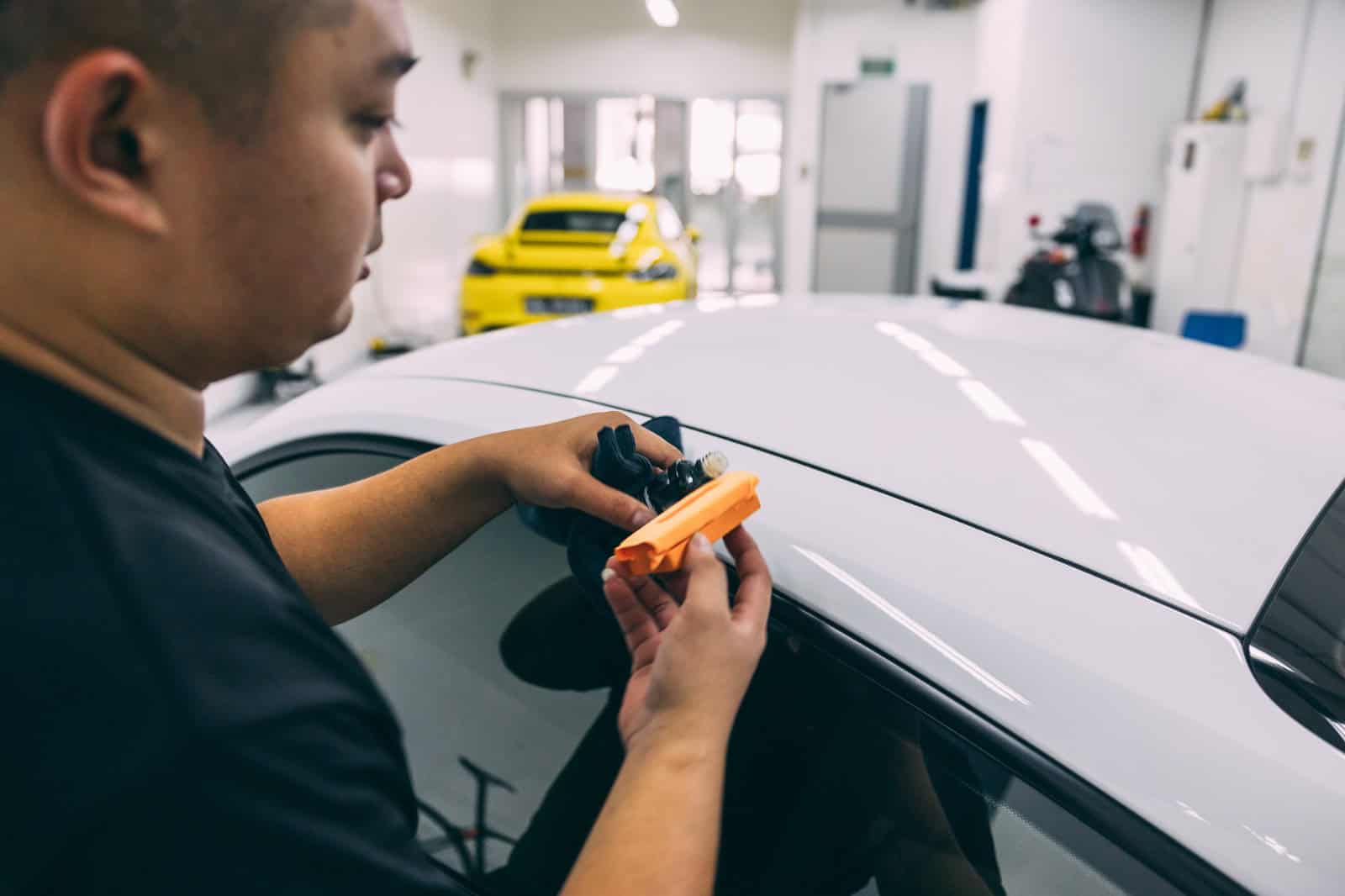 Technician applying PPF film on car's hood during full detailing process.