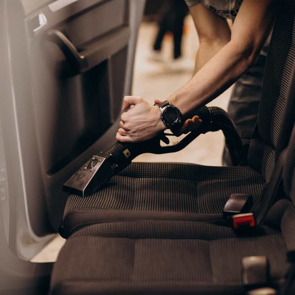 Person disinfecting car seat with cleaning equipment for interior hygiene.