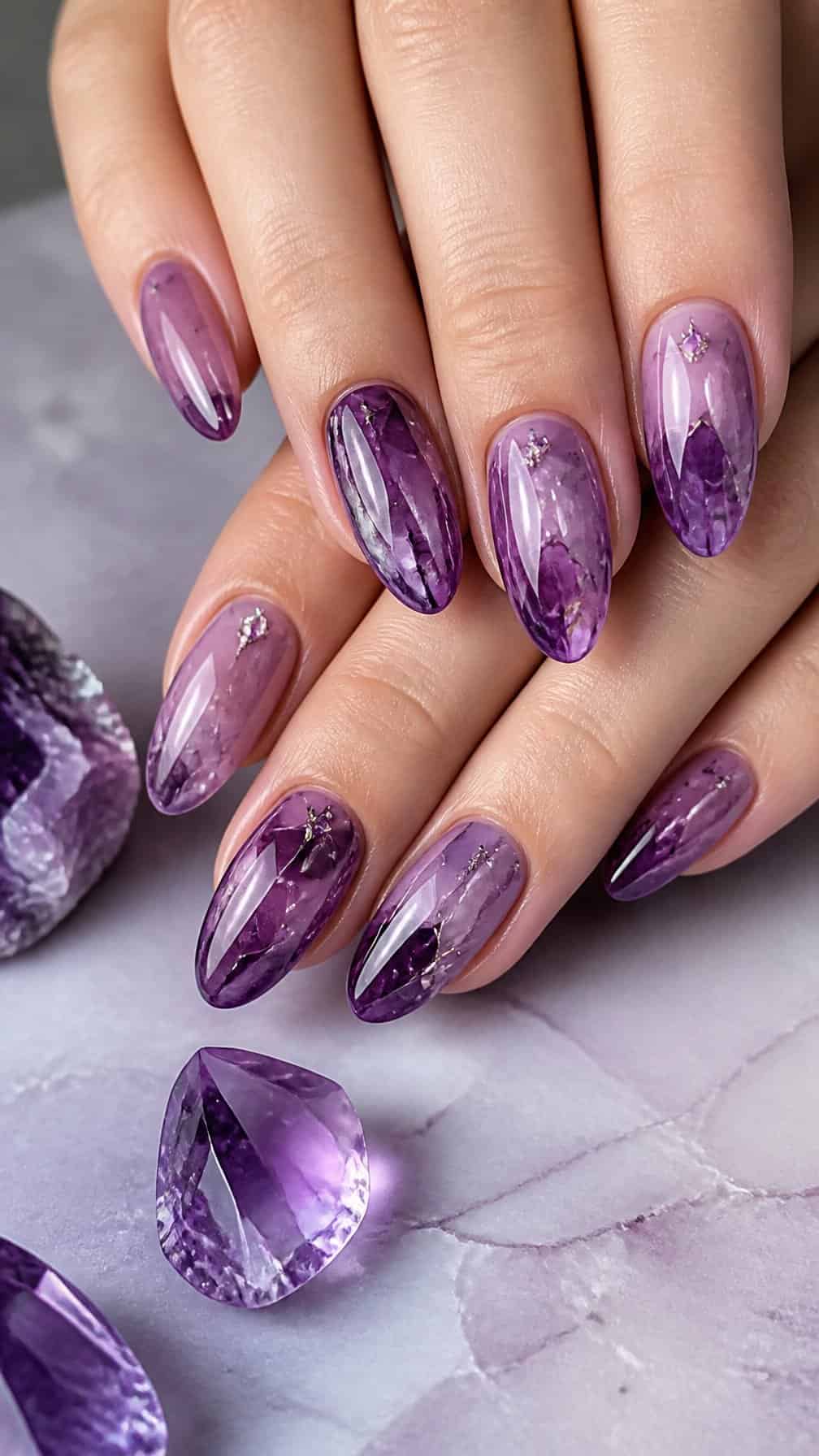 A hand displays glossy purple nails decorated with amethyst-inspired crystal patterns.
