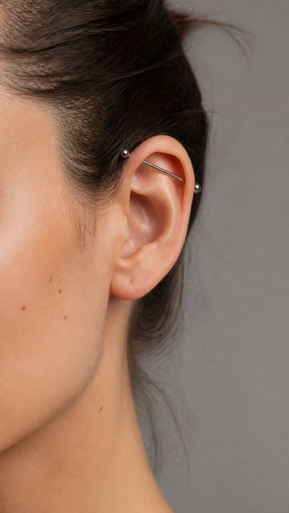 Close-up of an adult ear with a simple industrial barbell piercing through the upper cartilage.