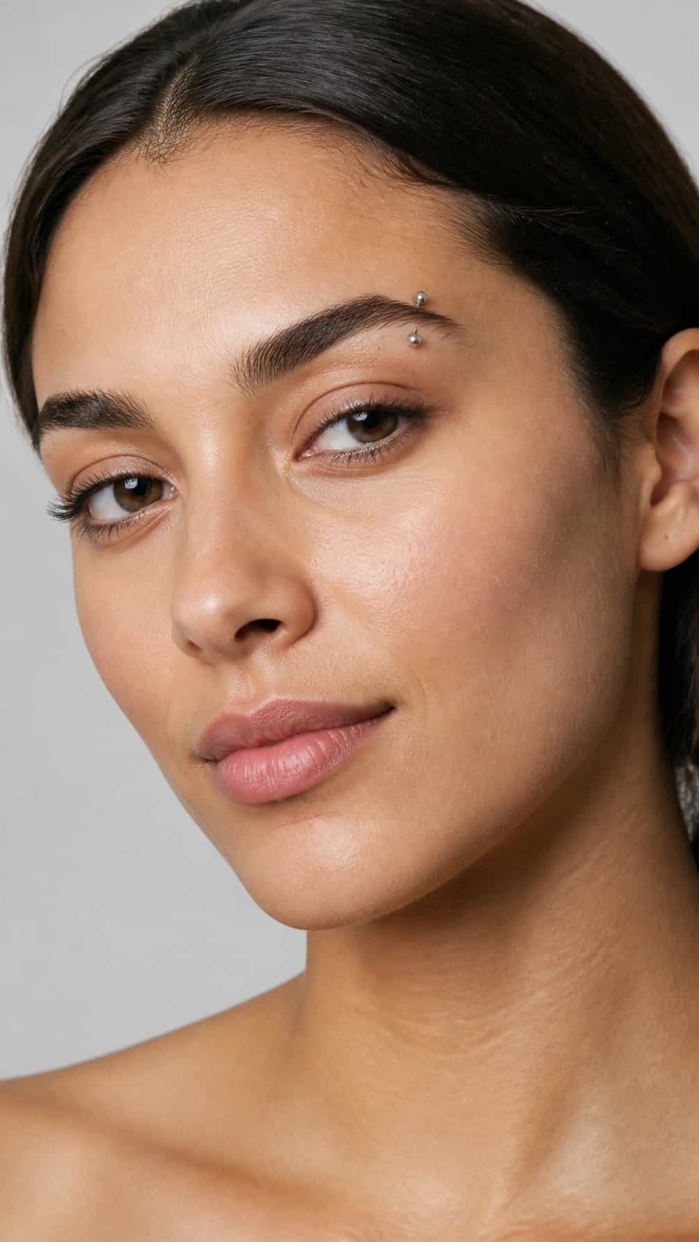 Close-up portrait of an adult with an arched eyebrow piercing above the outer brow.