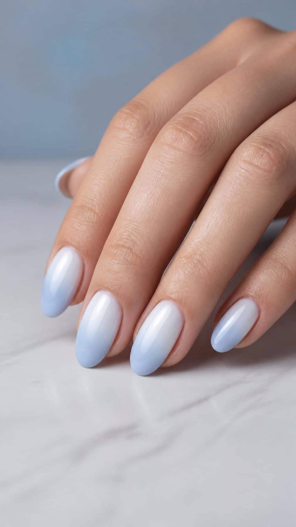 A close-up of manicured hands with glossy baby blue and white ombre nails.