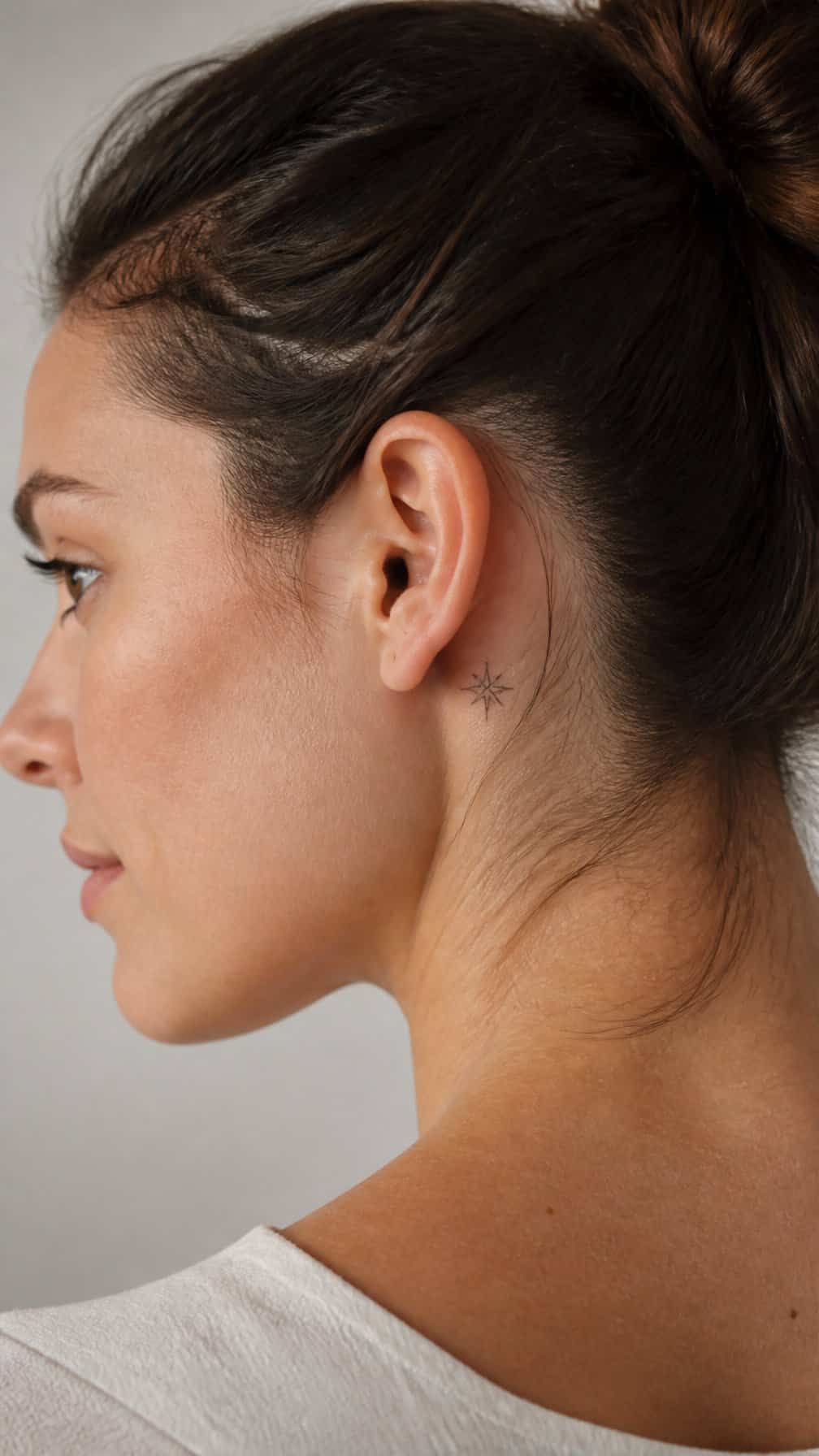 Close-up of a woman showing a small tattoo behind her ear.